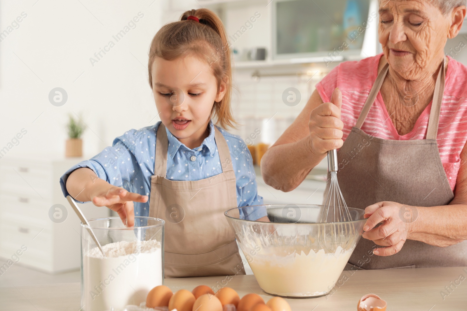 Photo of Cute girl and her grandmother cooking in kitchen