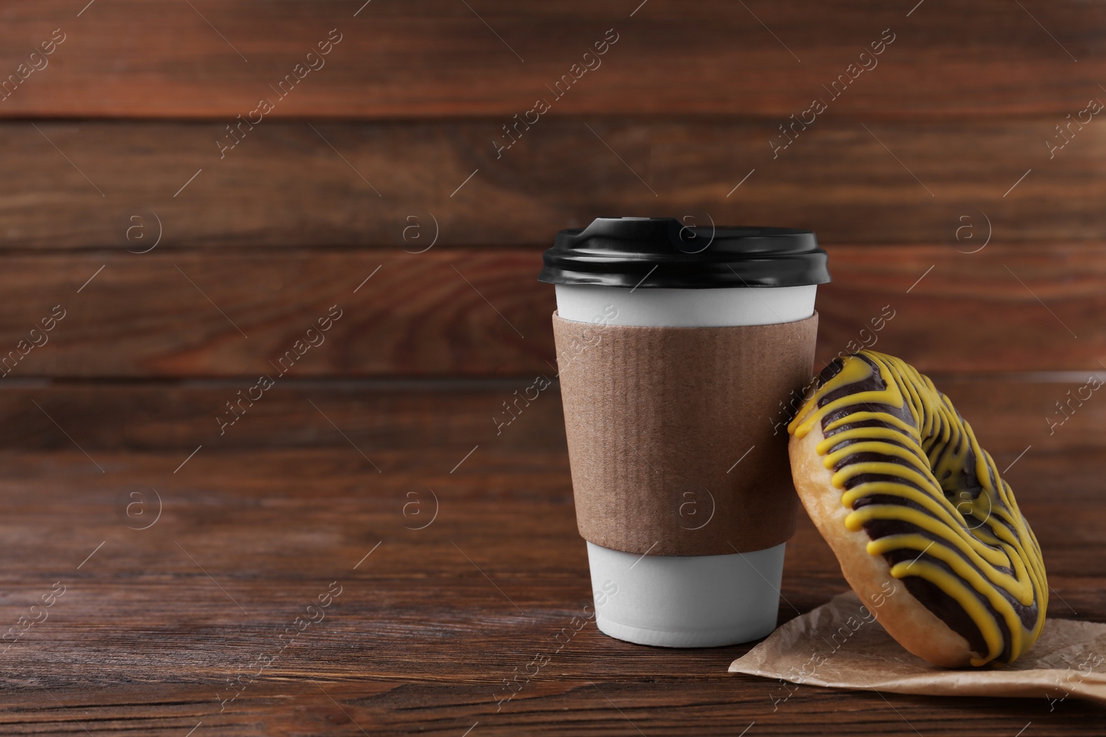 Photo of Tasty frosted donut and hot drink on wooden table, space for text