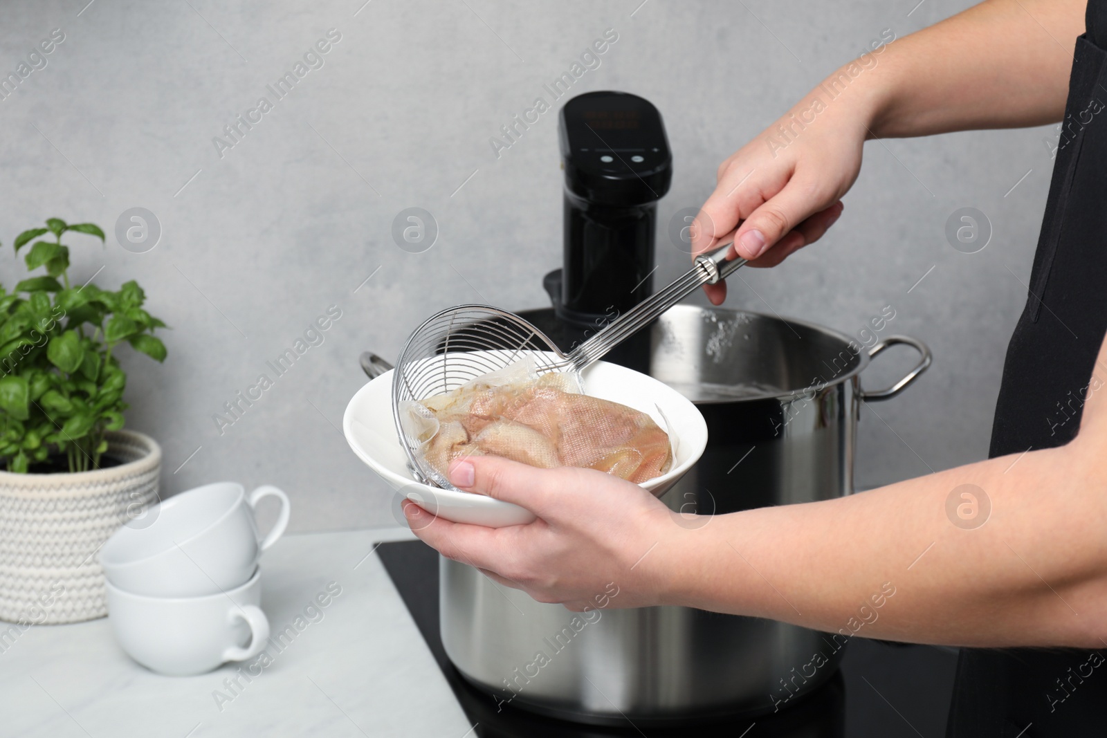 Photo of Woman taking out vacuum packed meat from pot in kitchen, closeup. Thermal immersion circulator for sous vide cooking