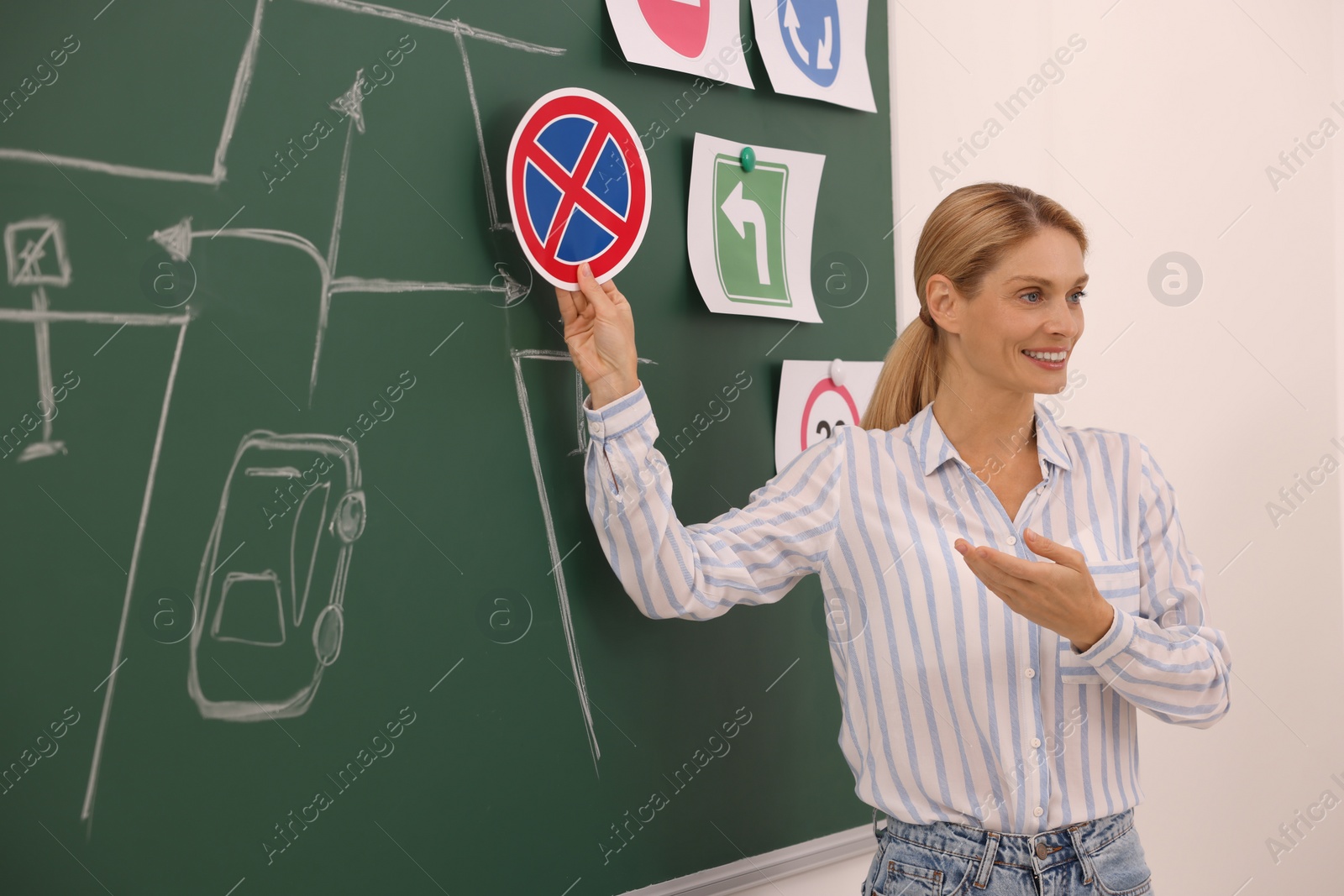 Photo of Teacher showing No Stopping road sign near chalkboard during lesson in driving school