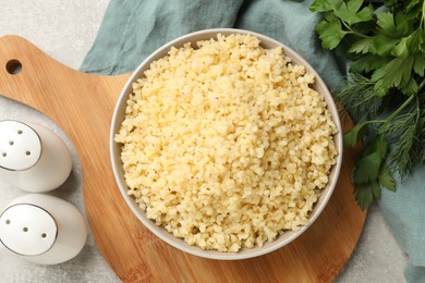 Delicious bulgur in bowl and spices on table, flat lay