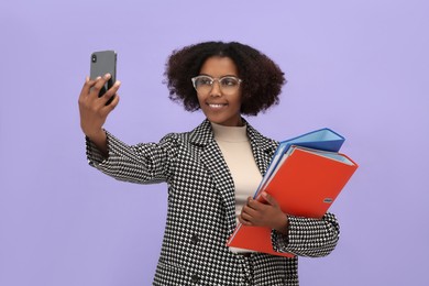 Photo of African American intern with folders taking selfie on purple background