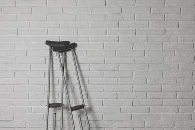 Pair of axillary crutches near white brick wall. Space for text