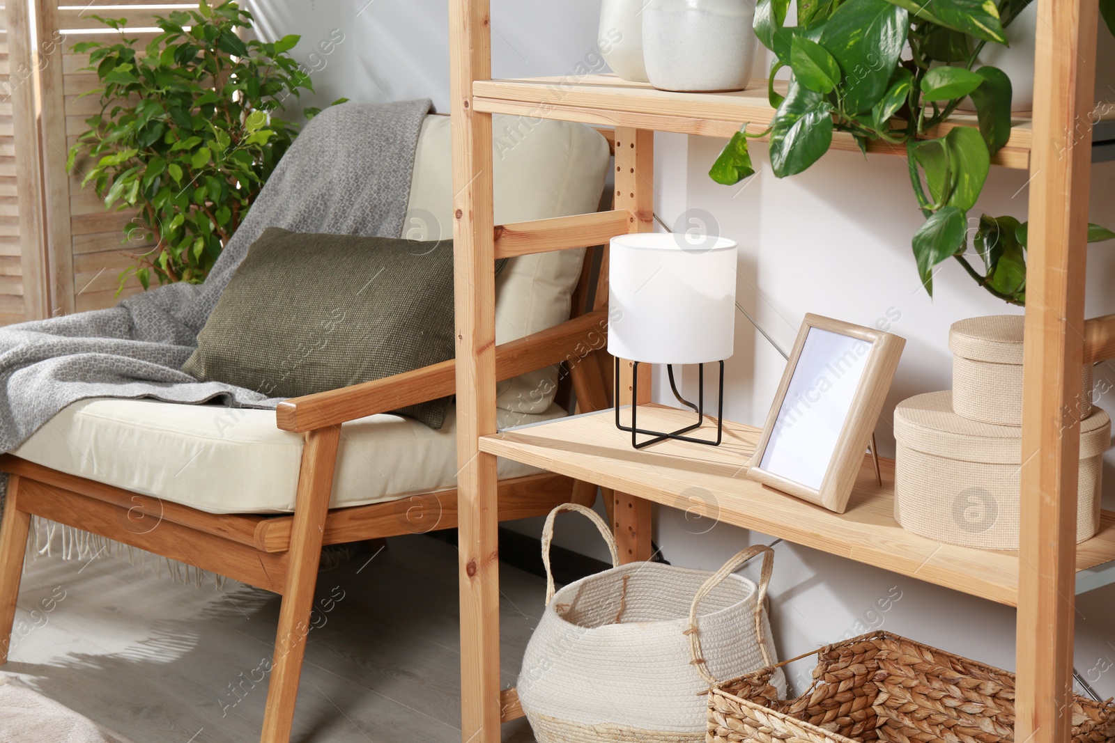 Photo of Wooden shelving unit with home decor, folding screen and armchair near light wall in room. Interior design