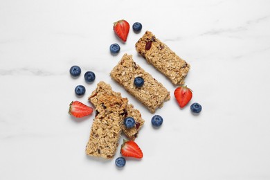 Tasty granola bars and berries on white marble table, flat lay
