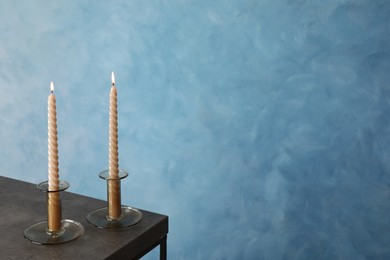 Holders with burning candles on black table near light blue wall, space for text