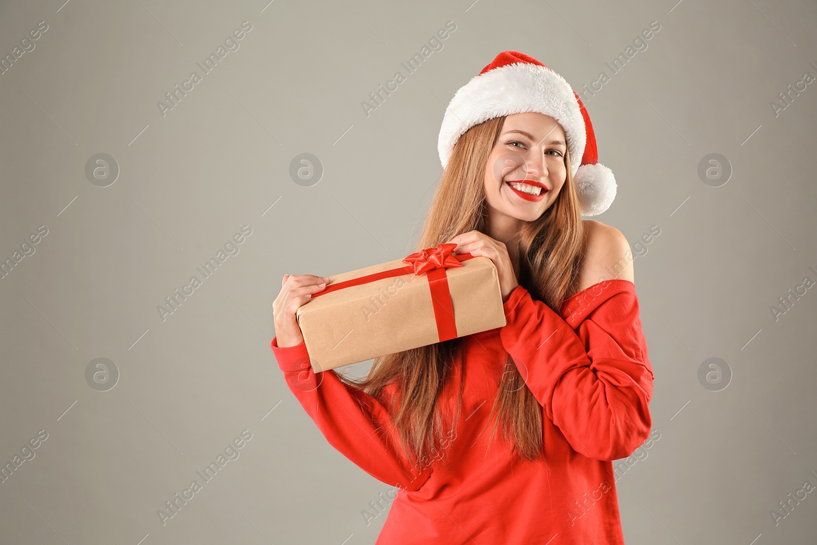 Photo of Young beautiful woman in Santa hat with gift box on grey background. Christmas celebration