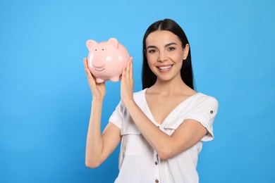Happy young woman with piggy bank on light blue background
