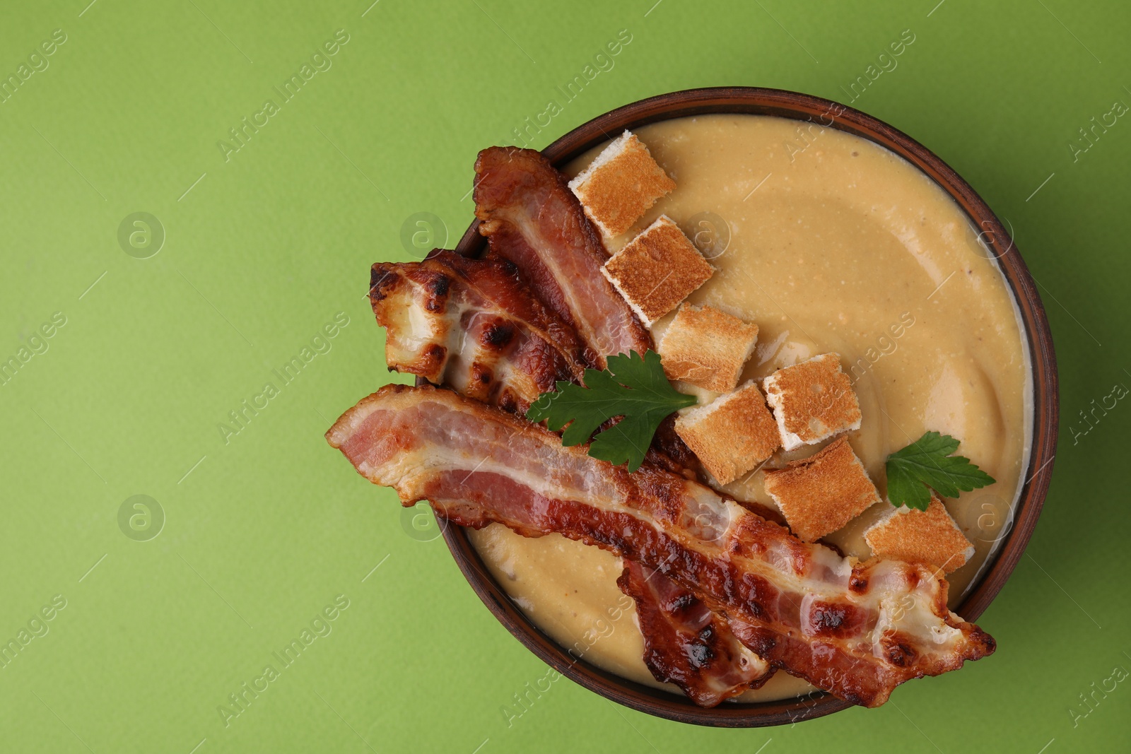 Photo of Delicious lentil soup with bacon and parsley in bowl on green table, top view. Space for text