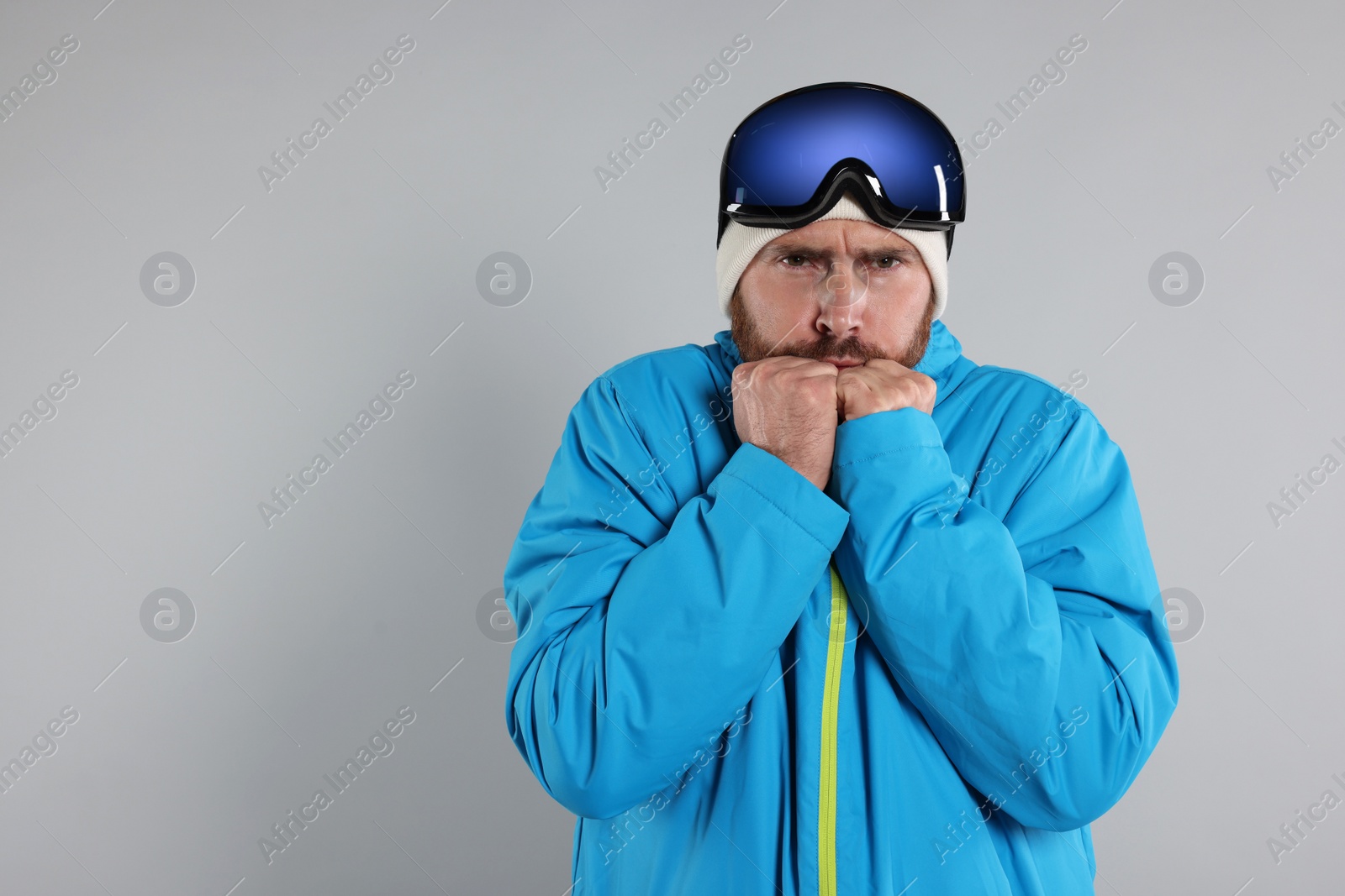 Photo of Winter sports. Man in ski suit and goggles on gray background, space for text