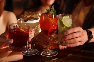 Photo of Friends clinking glasses with fresh cocktails in bar, closeup