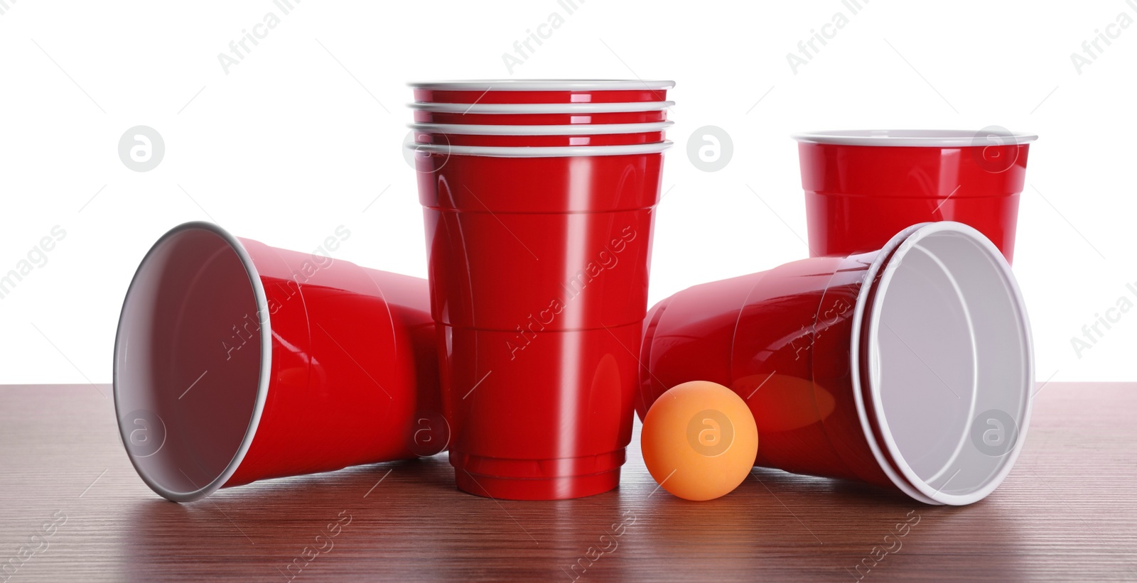 Photo of Plastic cups and ball for beer pong on wooden table against white background