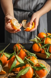 Photo of Woman peeling ripe tangerine over table, closeup