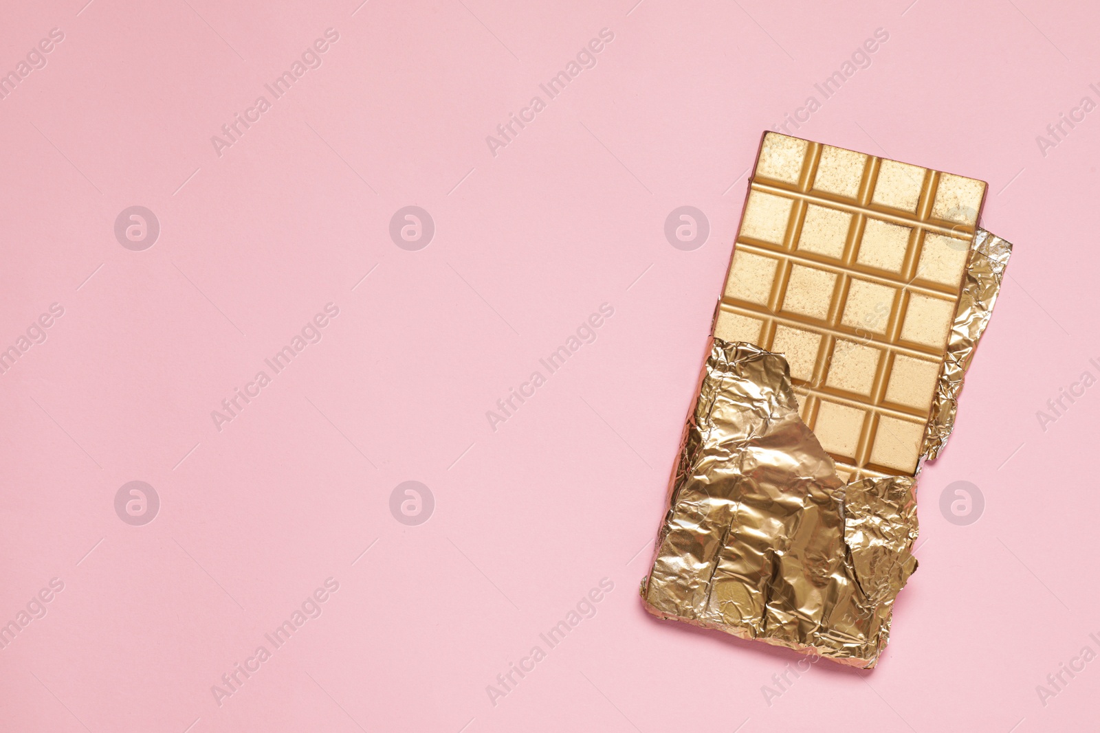 Photo of Shiny golden chocolate bar with foil on pink background, top view. Space for text
