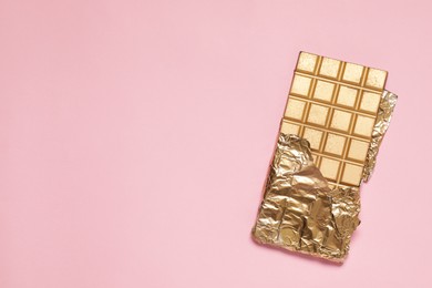 Photo of Shiny golden chocolate bar with foil on pink background, top view. Space for text