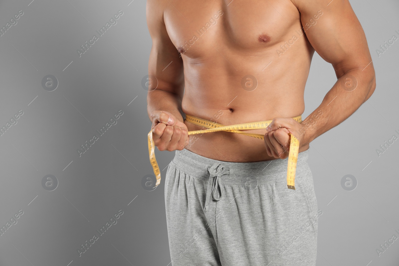 Photo of Young man with slim body using measuring tape on grey background, closeup view. Space for text