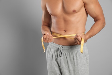 Photo of Young man with slim body using measuring tape on grey background, closeup view. Space for text