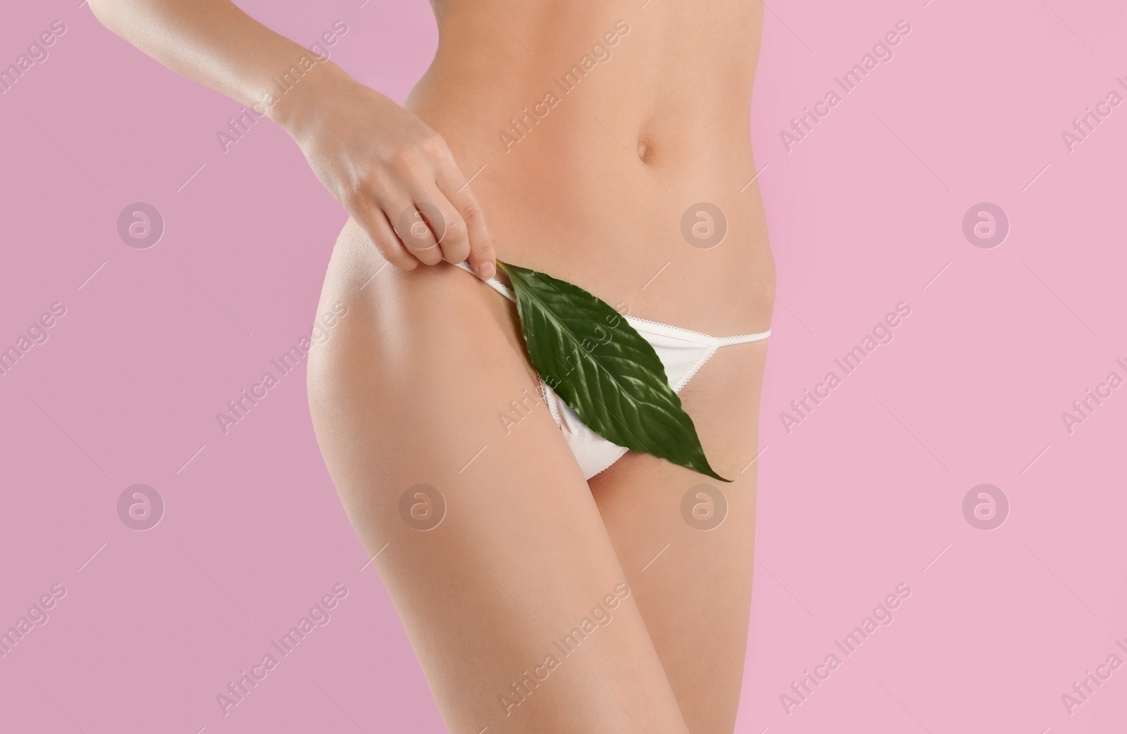 Photo of Woman with leaf showing smooth skin after Brazilian bikini epilation on pink background, closeup. Body care concept