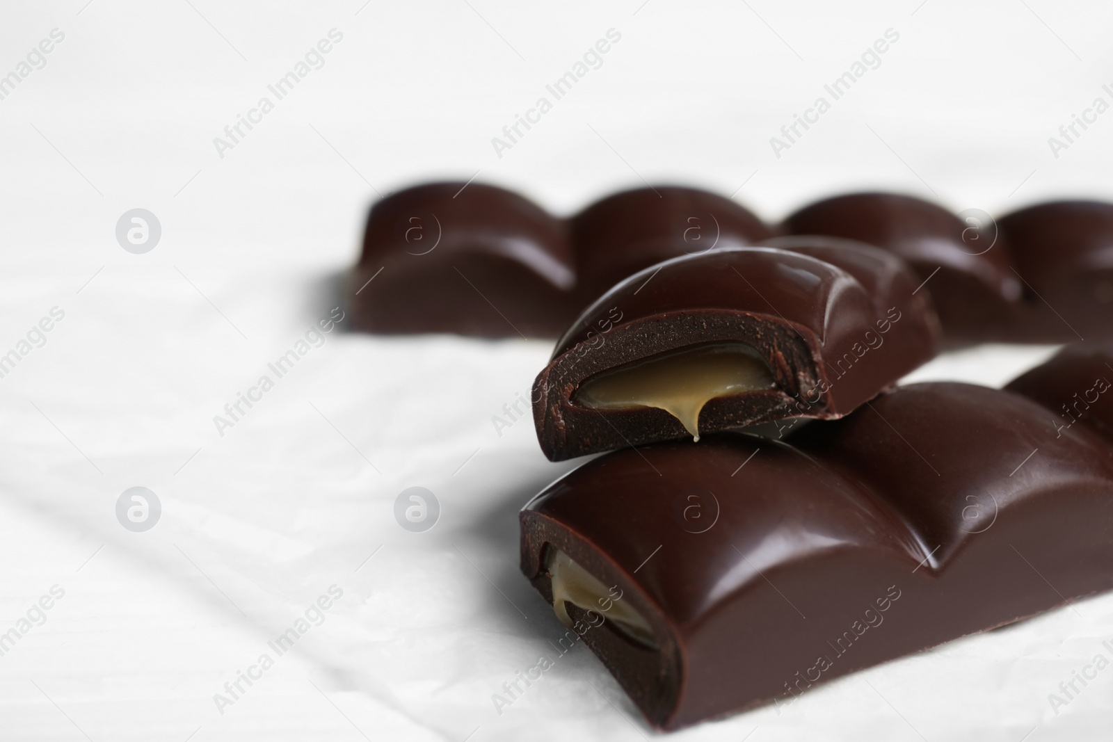 Photo of Pieces of chocolate with caramel filling on white table, closeup. Space for text