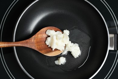 Frying pan with coconut oil and wooden spatula on induction stove, top view. Healthy cooking