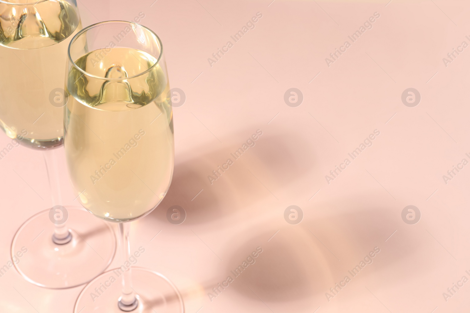 Photo of Glasses of delicious sparkling wine on pale pink background, closeup. Space for text