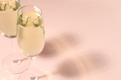 Glasses of delicious sparkling wine on pale pink background, closeup. Space for text