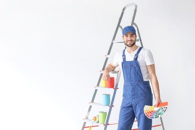 Male decorator with color palette near ladder on white background