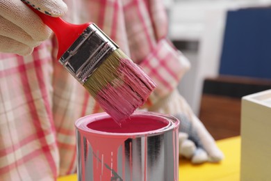 Photo of Woman dipping brush into can of pink paint, closeup