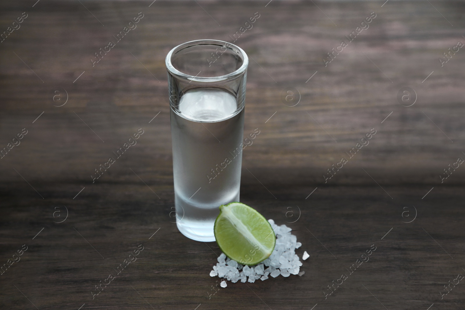 Photo of Mexican tequila shot with lime slice and salt on wooden table. Drink made from agave