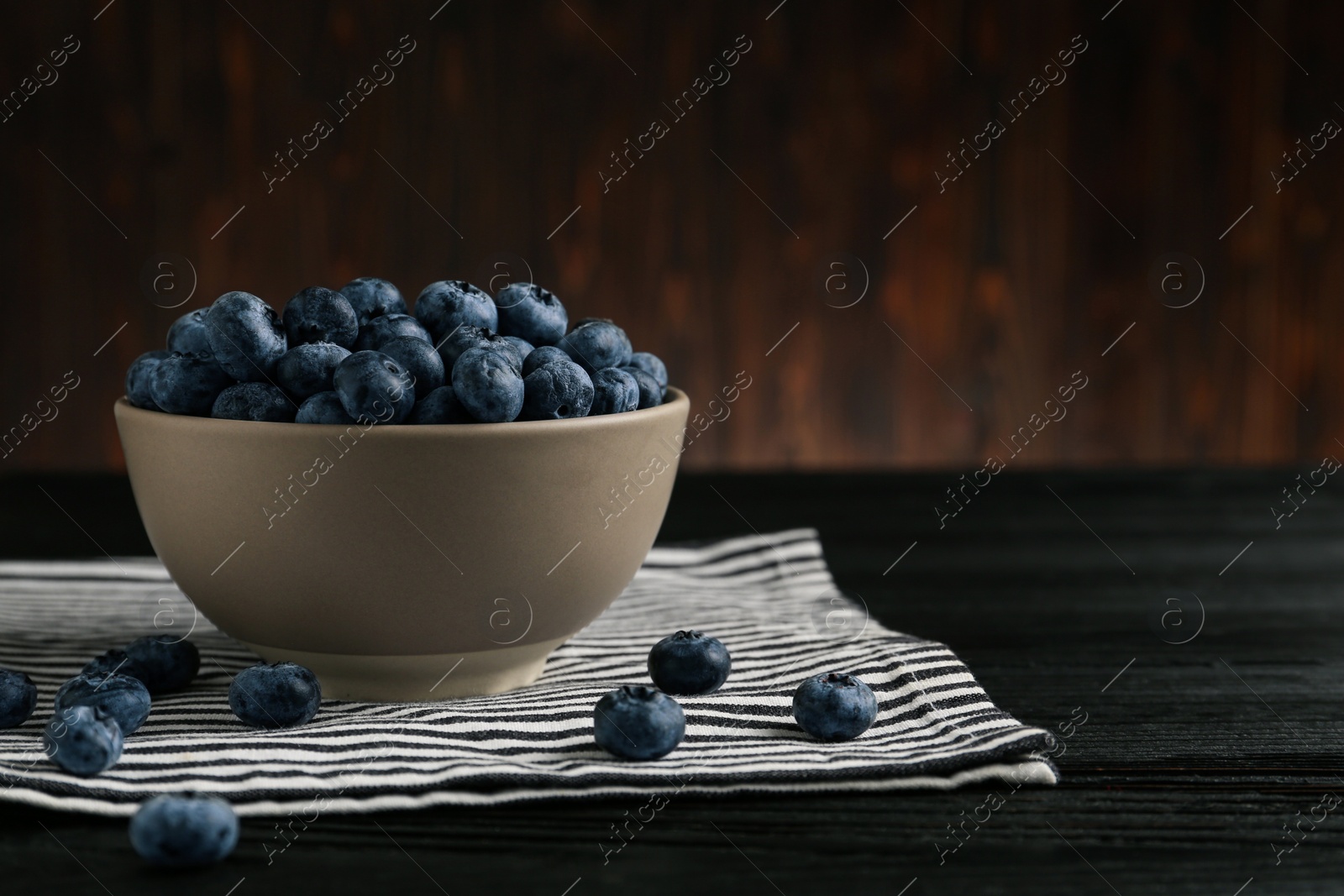 Photo of Ceramic bowl with blueberries on black wooden table, space for text. Cooking utensil