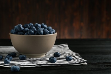 Photo of Ceramic bowl with blueberries on black wooden table, space for text. Cooking utensil