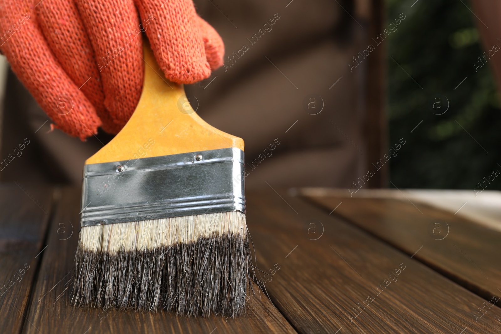 Photo of Man applying wood stain onto wooden surface against blurred background, closeup. Space for text