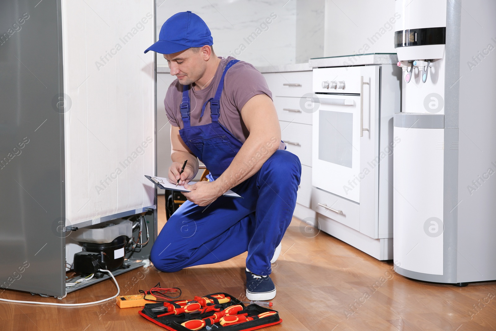 Photo of Male technician with clipboard examining broken refrigerator in kitchen