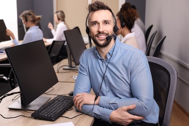 Photo of Call center operator with headset and his colleagues working in modern office