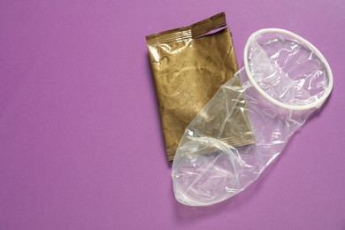 Photo of Unrolled female condom and torn package on violet background, above view with space for text. Safe sex