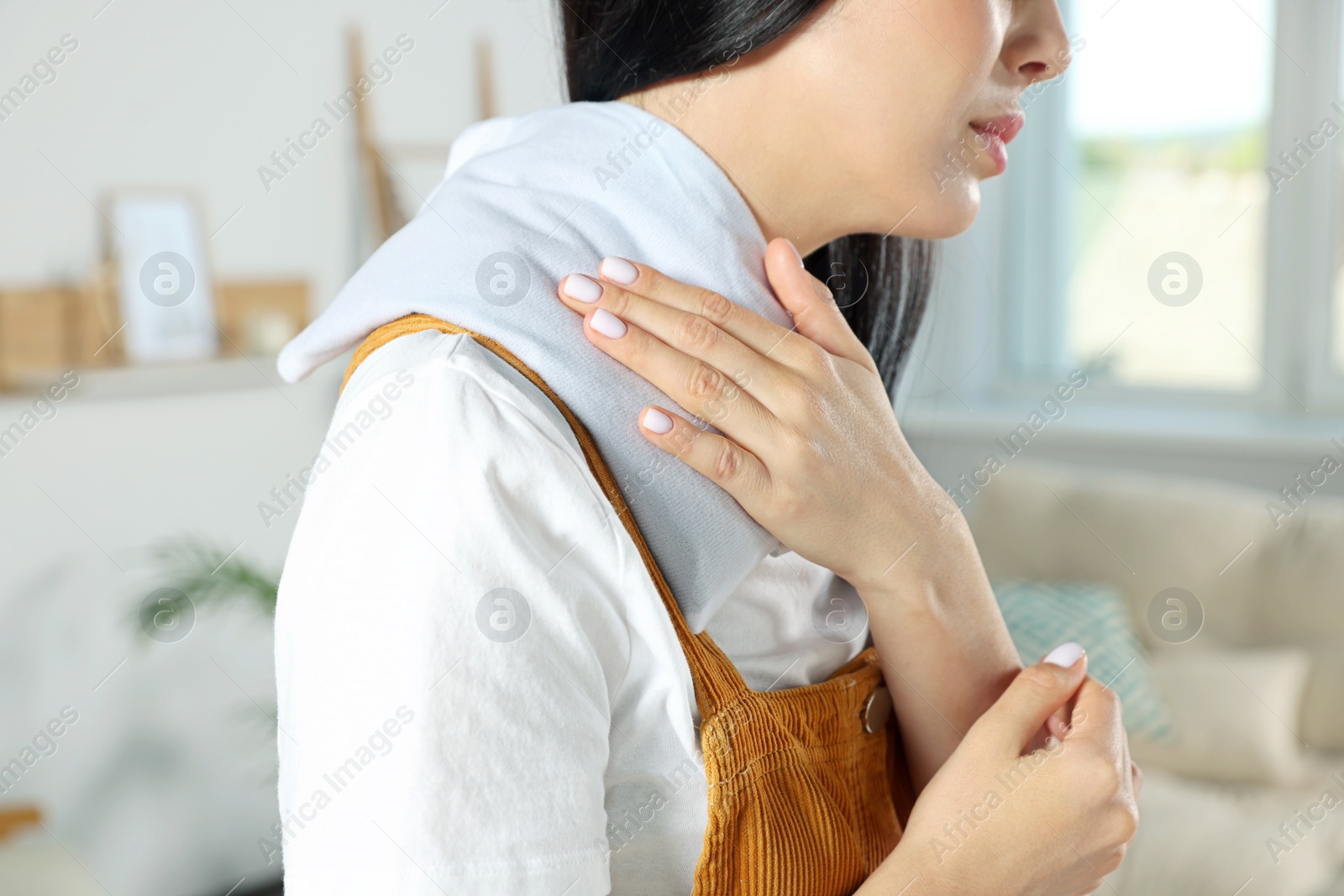 Photo of Young woman using heating pad on neck at home, closeup