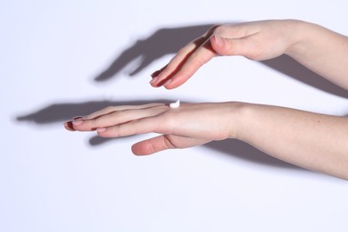 Woman applying cream on her hand against white background, closeup