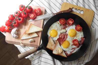 Photo of Delicious fried eggs with bacon and tomatoes in pan on table, flat lay