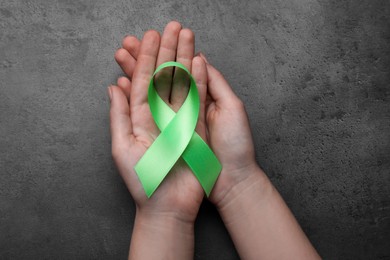 Photo of World Mental Health Day. Woman holding green ribbon on black background, top view