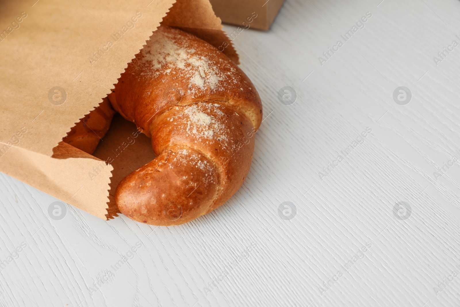 Photo of Paper bag with pastry on light wooden background. Space for text
