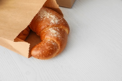 Paper bag with pastry on light wooden background. Space for text