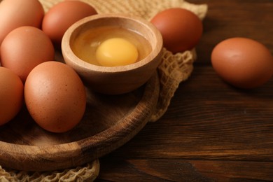 Raw chicken eggs and bowl with yolk on wooden table, closeup