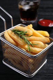 Photo of Frying basket with tasty french fries and rosemary on dark wooden table, closeup