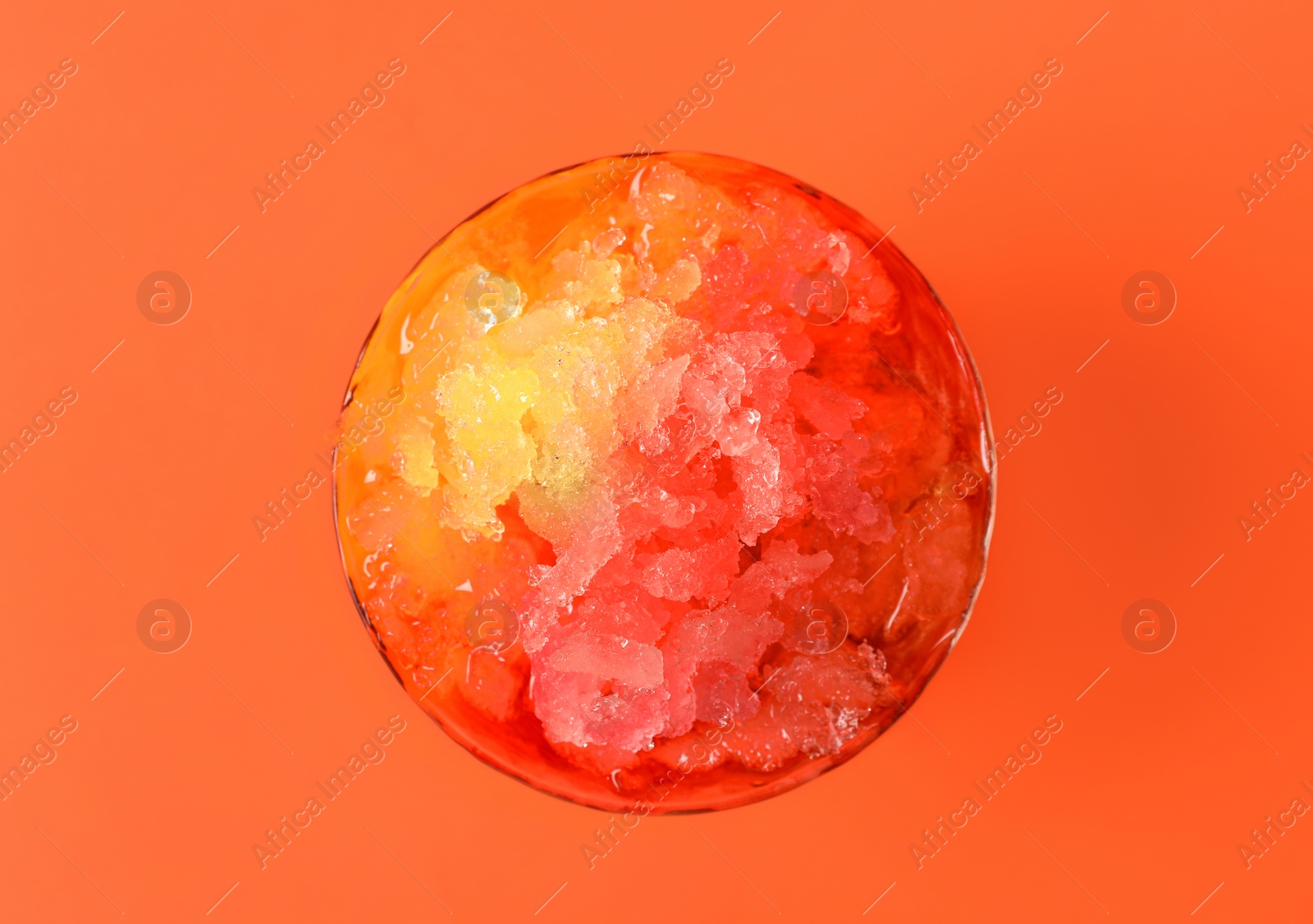 Photo of Rainbow shaving ice in glass dessert bowl on orange background, top view