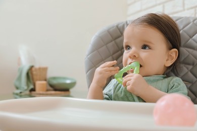 Photo of Cute little baby nibbling teether in high chair indoors. Space for text