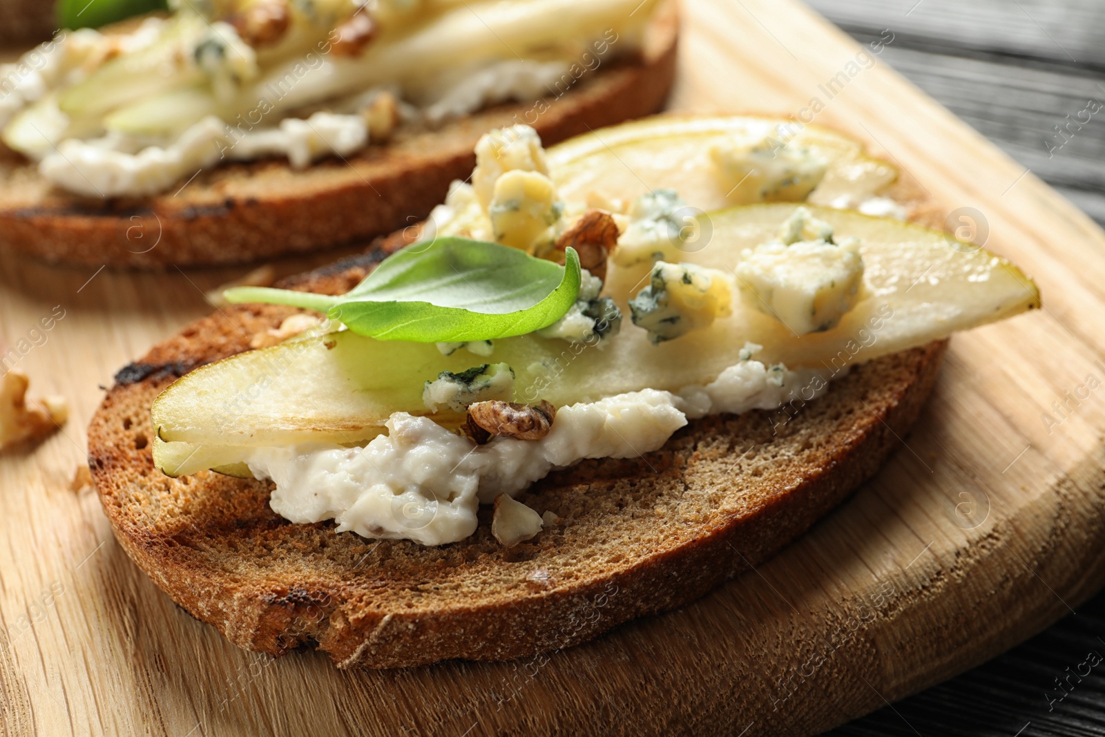 Photo of Wooden board with delicious pear bruschetta on table, closeup