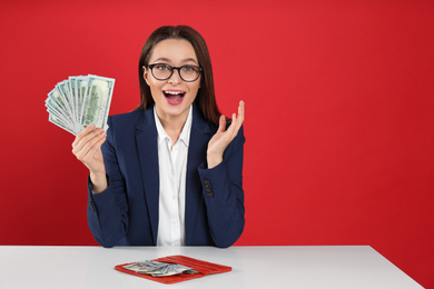 Photo of Emotional young woman with money and wallet at table on crimson background