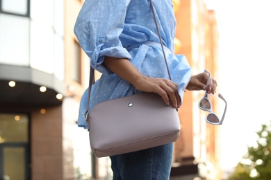 Photo of Young woman with stylish bag and sunglasses on city street, closeup