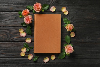 Photo of Flat lay composition with closed hardcover book and flowers on black wooden table