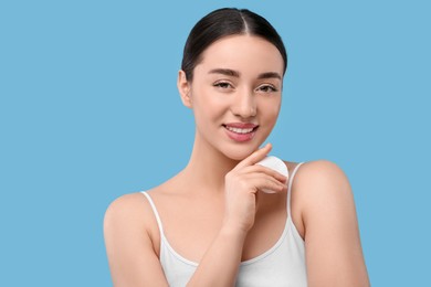 Photo of Beautiful woman with cotton pad on light blue background. Makeup removal